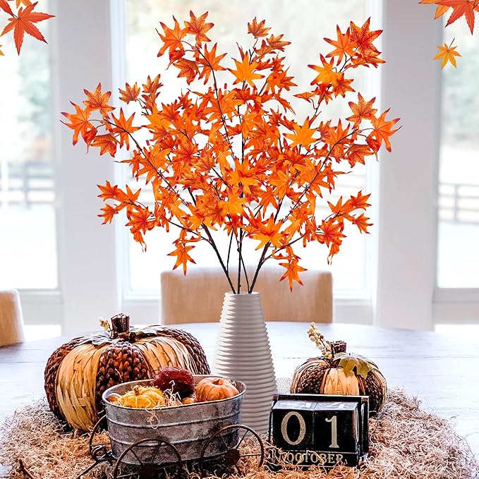 Kunstzweige mit orangefarbenen Ahornblättern in weißer Vase auf herbstlich dekoriertem Tisch – daneben Kürbisse, Drahtwagen mit Deko, Kalenderblock ‚01 Oktober‘ – warme, saisonale Stimmung