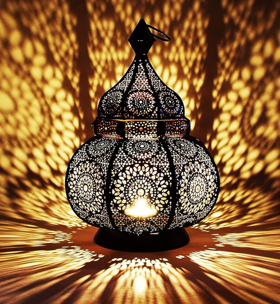 Schwarze orientalische Metalllaterne mit kunstvollem Muster und brennendem Teelicht im Inneren – wirft warme, ornamentartige Lichtreflexe auf die Wand, dekorativ im Herbstambiente